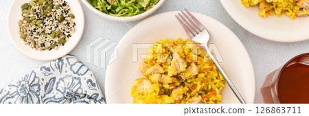Stewed rice with chicken breast and mixed salad with radishes and various seeds, a served table with food and a vase of flowers Stewed rice with chicken breast and mixed salad with radishes and various seeds, a served table with food and a vase of flowers 126863711
