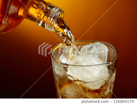 Bottle of whiskey pouring into a glass with ice. 126864174