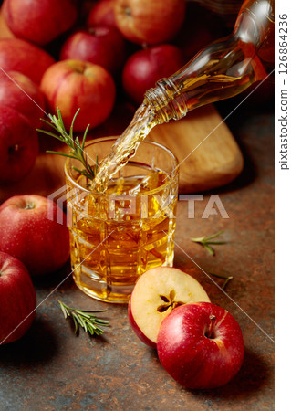 Apple cider is poured from a bottle into a glass. Apple cider is poured from a bottle into a glass. 126864236