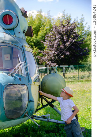 A child stand near an old plane and dreams of becoming a pilot when he grows up. The concept of choosing a future profession. A child stand near an old plane and dreams of becoming a pilot when he grows up. The concept of choosing a future profession. 126864243