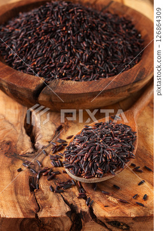 Natural black rice in a wooden bowl and spoon on a wooden surface in rustic style, top view 126864309