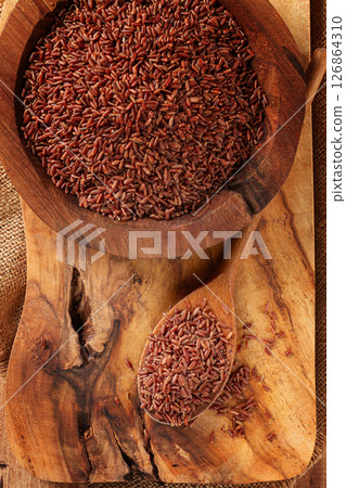 Natural red rice, in a wooden bowl and spoon on a wooden surface in rustic style, top view Natural red rice, in a wooden bowl and spoon on a wooden surface in rustic style, top view 126864310