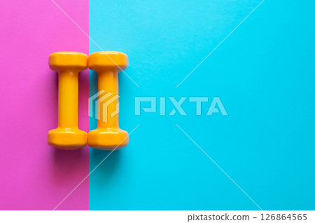 Two orange dumbbells on a pink and blue background with copy space. A tool for training, sport and activity in summer time. 126864565