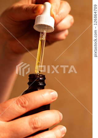 Close up of female hand carefully dropping aromatic body oil with glass pipette. Spa treatments aromatherapy self care concept. International Self Care Day 126864709