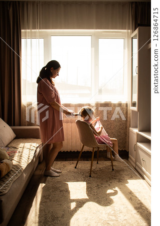 Mother gently braids her 4 years old daughter hair in sweet bonding moment. Perfect for parenting, childhood, and family lifestyle concepts. 126864715