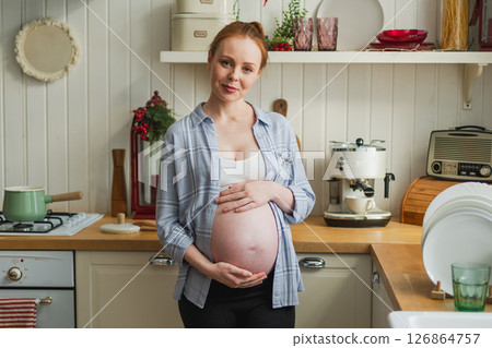 Pregnancy motherhood people expectation future. Pregnant woman with big belly smiling in kitchen at home. Girl hugging her tummy enjoying pregnancy. Maternity tenderness parenthood new life concept Pregnancy motherhood people expectation future. Pregnant woman with big belly smiling in kitchen at home. Girl hugging her tummy enjoying pregnancy. Maternity tenderness parenthood new life concept 126864757