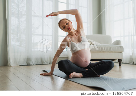 Pregnancy yoga fitness workout training. Pregnant woman practicing yoga at home. Pregnant girl doing sports exercise on yoga mat indoor. Woman with big belly have fitness training practicing asana 126864767