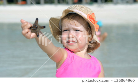 Baby girl holds starfish while relaxing on tropical beach with family 126864960