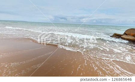 The Serene Beach Features Gentle Waves and a Beautiful Sandy Shoreline Beneath a Cloudy Sky 126865646