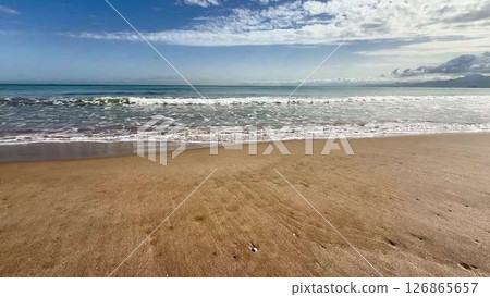 Enjoy a serene beach view showcasing rolling waves, a vibrant blue sky, and tranquility 126865657