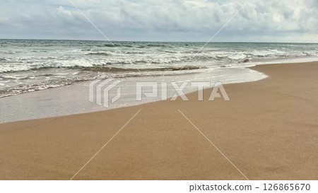 A Serene Beach Scene Featuring Gentle Ocean Waves, Fluffy Clouds, and Calm Skies 126865670