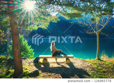 Young woman sitting on the bench under trees near lake at sunris 126865778