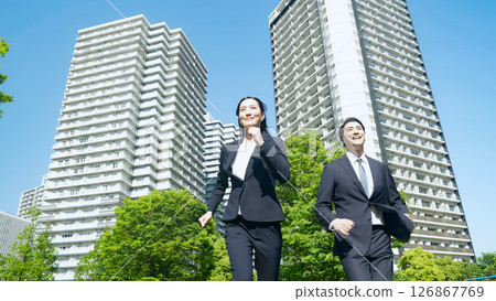 Male and female business people running through a city with fresh greenery 126867769