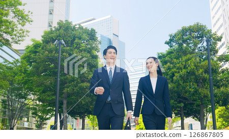 Male and female business people walking through a city with fresh greenery Male and female business people walking through a city with fresh greenery 126867805