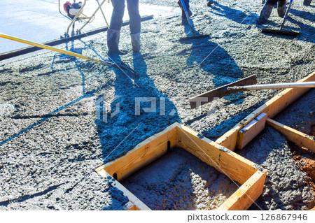 Construction workers are pouring concrete setting wooden frames for foundation in works day 126867946