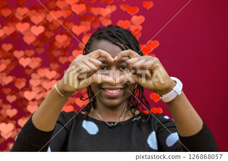 Smiling African Woman Making Heart Sign with Hands on Heart Bokeh Background Smiling African Woman Making Heart Sign with Hands on Heart Bokeh Background 126868057