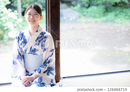 A woman in a yukata sitting on the veranda looks at the camera 126868719