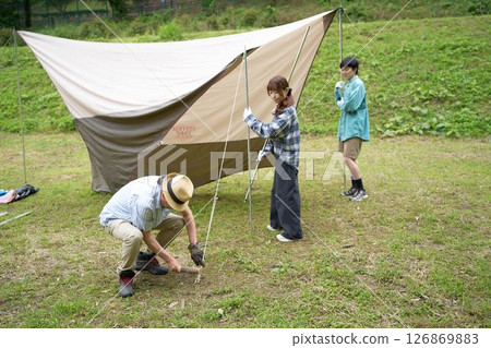 Camping friends setting up a tarp Camping friends setting up a tarp 126869883
