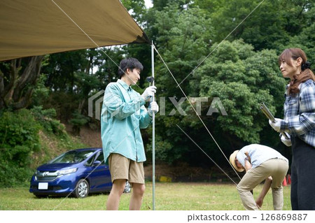 Camping friends setting up a tarp 126869887