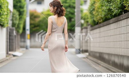 A style shot of a woman walking around town in a beige maxi dress A style shot of a woman walking around town in a beige maxi dress 126870540