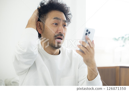 A man holding his head while looking at his smartphone 126871350