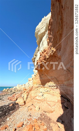 Colorful fossil rock formations rising on the seashore, creating dramatic contrast against clear blue sky, offering picturesque view of coastal geology 126871882
