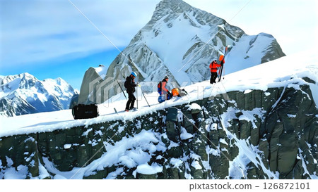 Skiers traversing rugged Alaskan mountain ridge, carrying skiing gear across pristine snowscape with towering peaks surrounding backcountry expedition 126872101