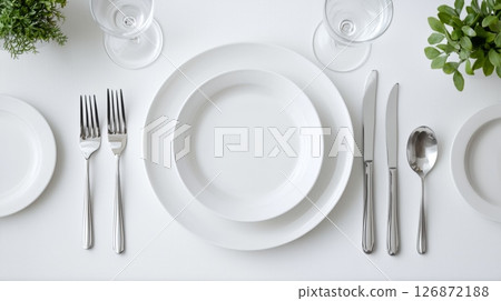 Elegant Dinner Table Setting with White Plates, Silver Cutlery, and Greenery on a White Background Elegant Dinner Table Setting with White Plates, Silver Cutlery, and Greenery on a White Background 126872188