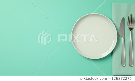 Elegant Dinner Setting with White Plate, Silverware, and Mint Green Background for Modern Dining Concepts Elegant Dinner Setting with White Plate, Silverware, and Mint Green Background for Modern Dining Concepts 126872275