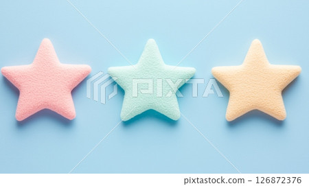 Three Colorful Star-Shaped Sponges on Light Blue Background - Pastel Pink, Green, and Yellow 126872376