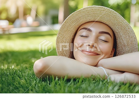 Serene woman in straw hat resting on green grass with closed eye 126872533