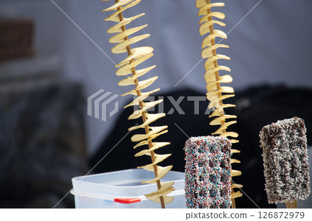 Spiral Potato Snacks and Colorful Dessert Sticks Displayed on Sticks at a Market Spiral Potato Snacks and Colorful Dessert Sticks Displayed on Sticks at a Market 126872979