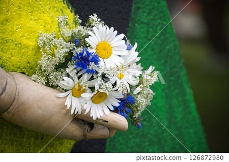Wooden hand tenderly holding a charming bouquet of vibrant daisies and blue flowers. 126872980