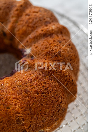 With precision, the bundt cake is carefully removed from the pan - placed onto a round cooling rack, preparing it for a flawless presentation and delightful indulgence. 126873968