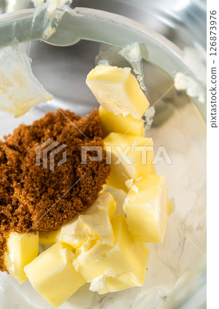 Butter and brown sugar are added to the mixing bowl, key ingredients for Chocolate Gingerbread Cookie Dough. These provide a creamy texture and deep sweetness, which complement the chocolate and 126873976