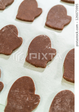 Close-up view of raw Pale Gingerbread Cookies in mitten shapes neatly arranged on a parchment-lined baking tray, ready for the oven. 126873995