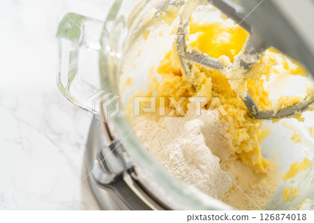 Close-up view of the stand mixer as dry ingredients are added to the wet mixture for Classic Sugar Cookie Dough. The flour is gently being incorporated into the butter, sugar, and eggs, creating the 126874018