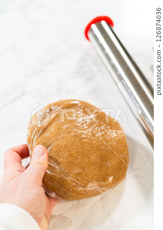 Straight-on view of hands holding amber gingerbread cookie dough wrapped in plastic wrap, showing preparation for chilling. Straight-on view of hands holding amber gingerbread cookie dough wrapped in plastic wrap, showing preparation for chilling. 126874036