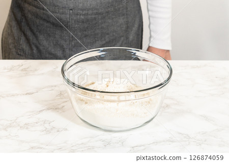 A glass mixing bowl filled with sifted flour for the Chocolate Gingerbread Cookie Dough recipe, placed on a marble countertop. The flour serves as the base for the cookie dough. A glass mixing bowl filled with sifted flour for the Chocolate Gingerbread Cookie Dough recipe, placed on a marble countertop. The flour serves as the base for the cookie dough. 126874059