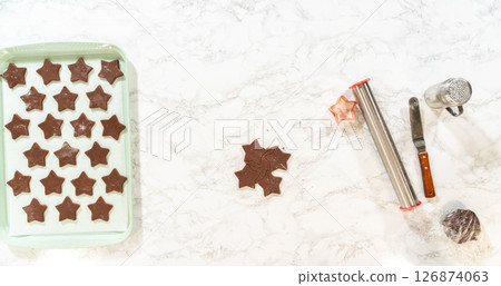 Overhead view of star-shaped chocolate cookies arranged on a parchment-lined baking sheet, ready for the oven. Overhead view of star-shaped chocolate cookies arranged on a parchment-lined baking sheet, ready for the oven. 126874063