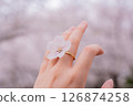A woman's hand wearing a cherry blossom ring with cherry blossoms in full bloom in the background 126874258