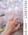 A woman's hand wearing a cherry blossom ring with cherry blossoms in full bloom in the background 126874260
