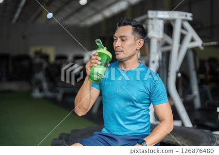 Fitness Hydration. A man savoring a drink from his protein shaker in the gym. Fitness Hydration. A man savoring a drink from his protein shaker in the gym. 126876480