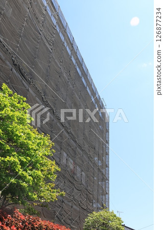 Apartment building covered with scaffolding and netting for exterior construction work Apartment building covered with scaffolding and netting for exterior construction work 126877234