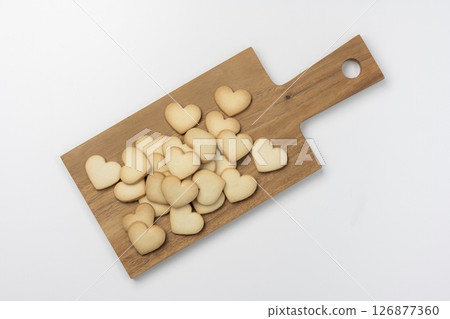 Overhead view of heart-shaped cookies and wooden cutting board on white background 126877360