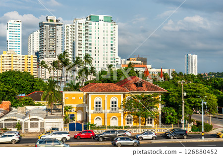 Colonial-style yellow house stands in contrast with the tall modern buildings of Cartagena, Colombia behind a busy street 126880452