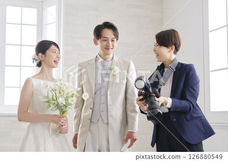 Smiling bride and groom and bridal photographer talking 126880549