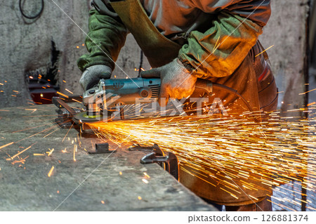 A detailed view of an angle grinder in action as it produces bright sparks while cutting metal in an industrial setting. 126881374