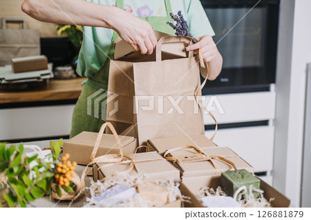Person wraps natural soaps in kraft packaging for a small business in a home kitchen. Handmade product packaging, creative process, DIY business visuals, home-based business 126881879