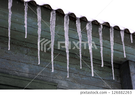 Winter icicles hanging from eaves of roof. 126882263